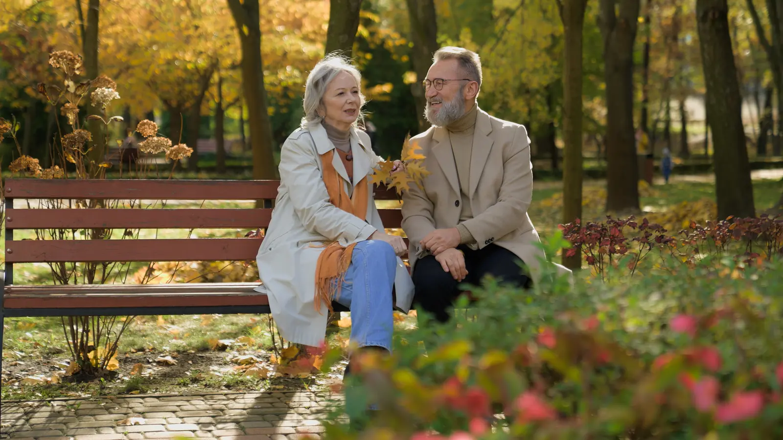 A couple talking on a park bench among autumn trees