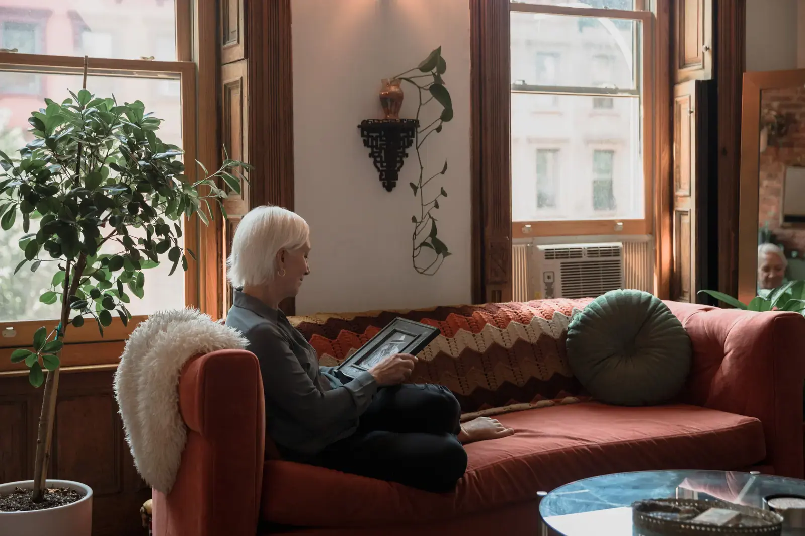 A woman sitting on a sofa at home, holding a framed photograph